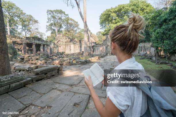 young woman reading guidebook at ancient temple in cambodia - guidebook stock pictures, royalty-free photos & images