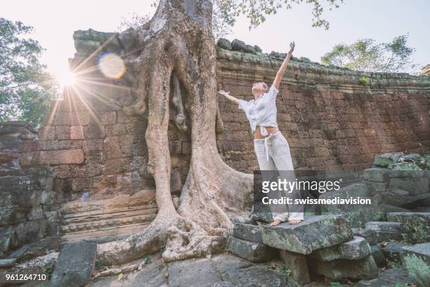 young woman arms outstretched at ancient temple near majestic tree roots - banteay kdei stock pictures, royalty-free photos & images