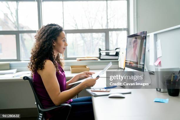 side view of businesswoman video conferencing with female colleague over desktop computer in office - woman business plan stock pictures, royalty-free photos & images