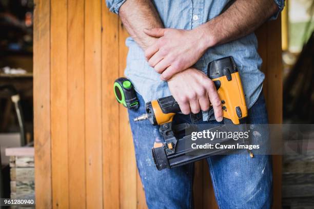 midsection of craftsperson holding nail gun while standing at workshop - 釘 ストックフォトと画像