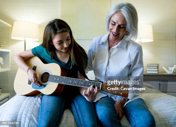 grandmother looking at granddaughter playing guitar while sitting on bed - plucking an instrument - fotografias e filmes do acervo