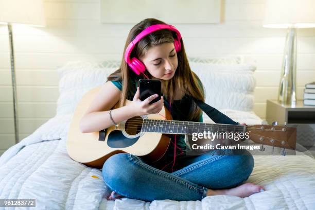 teenage girl using smart phone while playing guitar in bedroom - plucking an instrument - fotografias e filmes do acervo