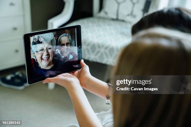 sisters video conferencing with grandparents through tablet computer at home - skypen stockfoto's en -beelden