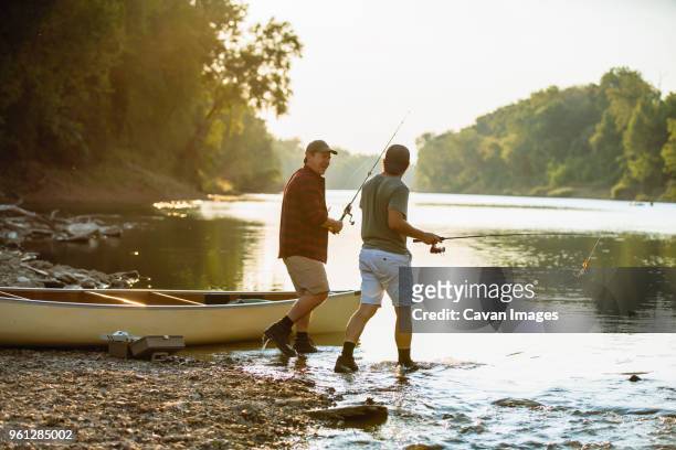 male friends holding fishing rods talking while walking at lakeshore - missouri mittlerer westen stock-fotos und bilder