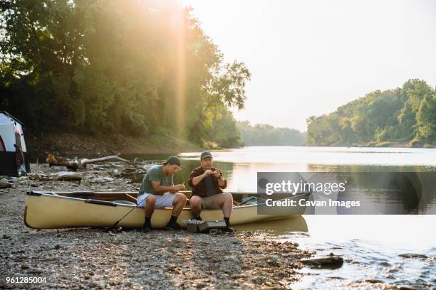 male friends adjusting fishing tackles while sitting on boat at campsite by lake - missouri lake stock pictures, royalty-free photos & images