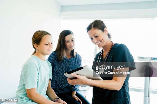 cheerful pediatrician showing tablet computer to mother and daughter sitting on examination table in hospital - 女性患者 ストックフォトと画像