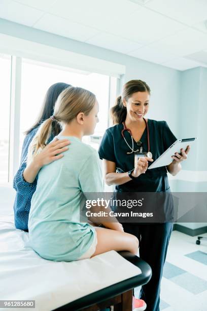 pediatrician showing tablet computer to mother and daughter sitting on examination table - caucasian doctor and nurse using tablet computer stock-fotos und bilder