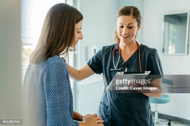 doctor consoling woman while showing tablet computer in medical examination room - adult patient with doctor and stethoscope foto e immagini stock