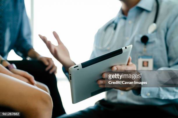 cropped hand of pediatrician showing tablet computer to mother and daughter in medical examination room - hands explaining stock pictures, royalty-free photos & images