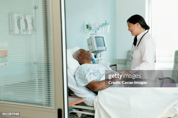 cheerful doctor talking to senior patient lying on bed in hospital ward - bed side view stock pictures, royalty-free photos & images