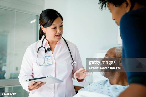 doctor with tablet computer talking to senior patient lying by daughter in hospital ward - three female doctors stock pictures, royalty-free photos & images