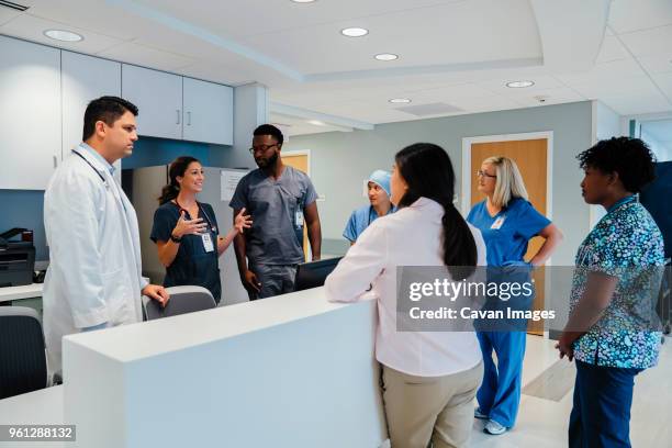 colleagues looking at female doctor explaining during meeting at hospital reception - health authority stock pictures, royalty-free photos & images