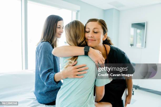 pediatrician embracing girl sitting by mother on examination table in hospital - doctors embracing stock pictures, royalty-free photos & images