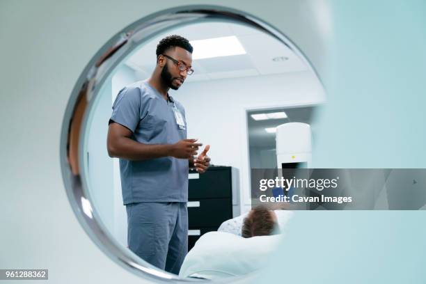 male nurse talking with patient lying in examination room seen through mri scanner - mri technician fotografías e imágenes de stock