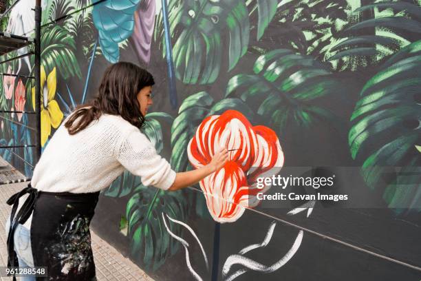 female artist painting mural on wall - murale foto e immagini stock