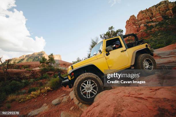 yellow off-road vehicle moving down on rocks at mountain against sky - vehículo de todo terreno fotografías e imágenes de stock