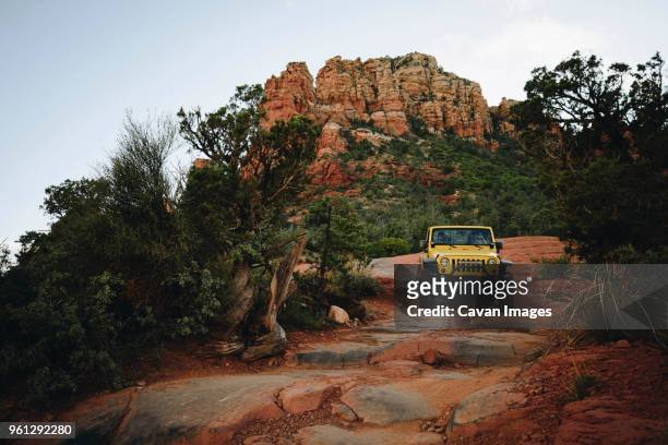 yellow off-road vehicle moving on rocks at mountains against sky - atv trail stock pictures, royalty-free photos & images