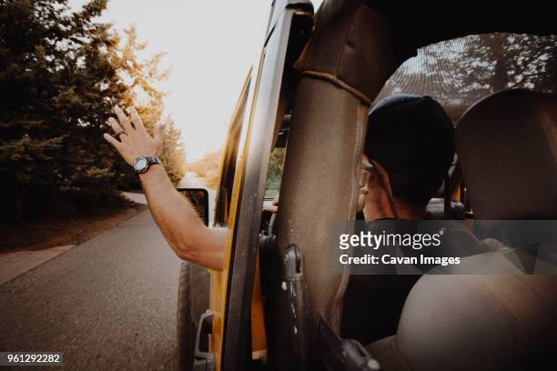 rear view of man waving through off-road vehicle window while driving on road - rear view hand window stockfoto's en -beelden