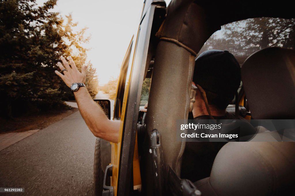 Rear view of man waving through off-road vehicle window while driving on road