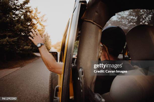 rear view of man waving through off-road vehicle window while driving on road - rear view hand window stock pictures, royalty-free photos & images