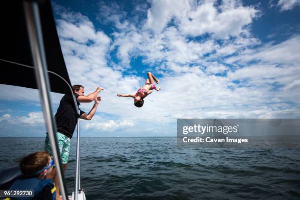 father and son looking at girl jumping into sea against cloudy sky - tampa day stock pictures, royalty-free photos & images