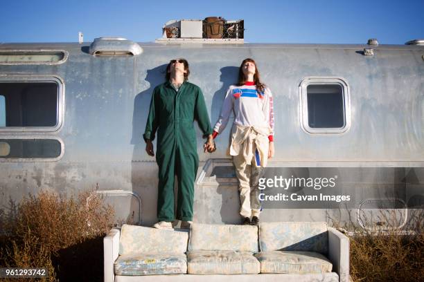 couple holding hands while standing on sofa by trailer home - vehicle trailer foto e immagini stock