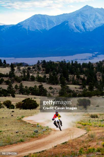 man riding motorcycle on dirt road against mountain - route moto stock-fotos und bilder