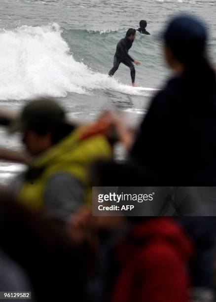 Surfer rides a wave as people barbeque on a beach during a spell of cool weather in Hong Kong on January 24, 2010. The northeast monsoon is bringing...