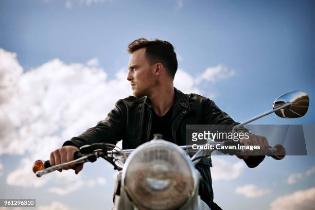 man looking away while riding motorcycle against sky - motociclista fotografías e imágenes de stock