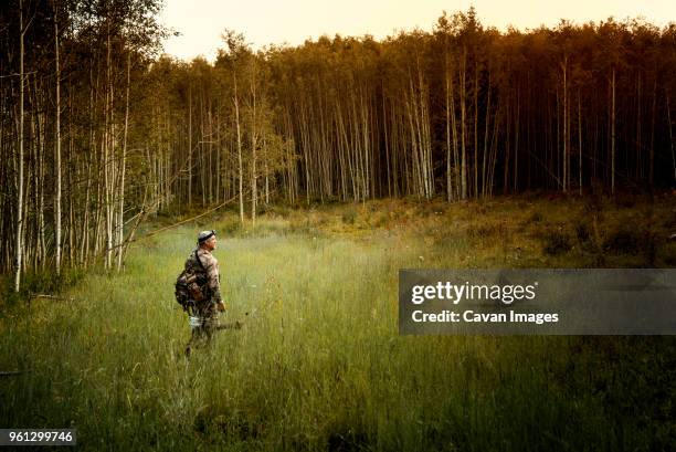 hunter with bow and arrow walking in forest - bow hunting stock pictures, royalty-free photos & images
