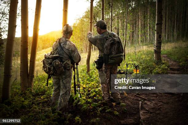 rear view of hunters discussing in forest - bow hunting stock pictures, royalty-free photos & images