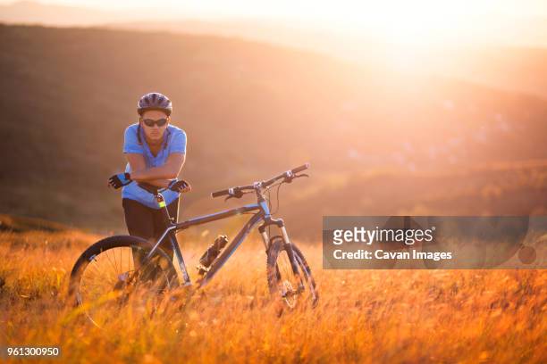 portrait of male athlete standing by bicycle on field during sunset - confidence male landscape stock-fotos und bilder