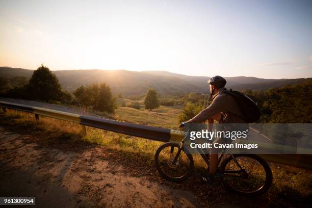 side view of male athlete with bicycle by guard rail against clear sky - confidence male landscape stock-fotos und bilder