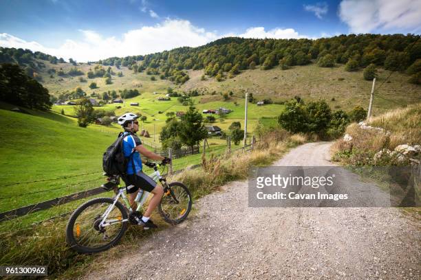 male athlete with bicycle on dirt road by field - confidence male landscape stock-fotos und bilder