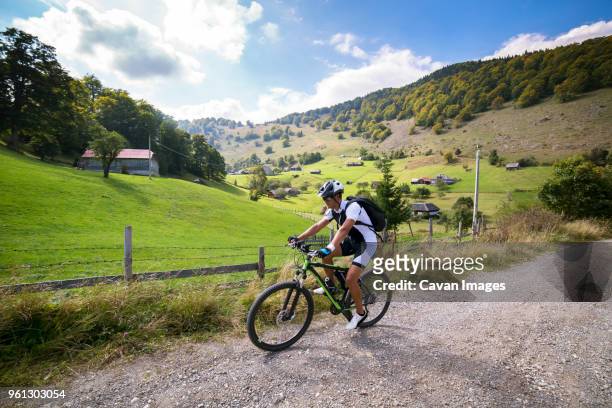 male athlete cycling on dirt road by field against sky - confidence male landscape stock-fotos und bilder