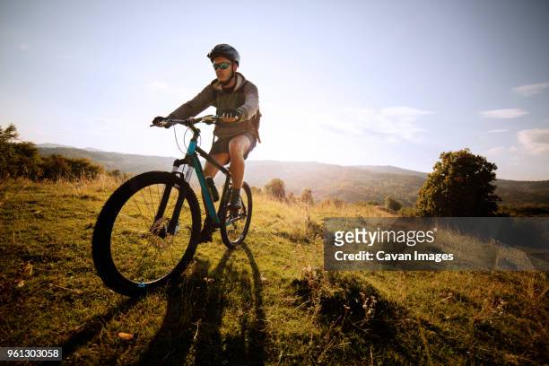 male athlete cycling on field against sky - confidence male landscape stock-fotos und bilder