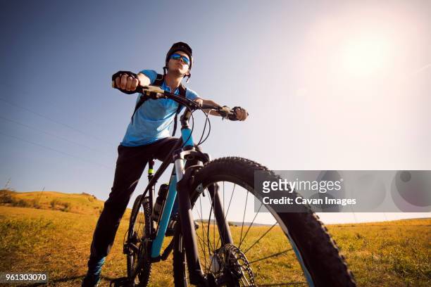 low angle view of male athlete on bicycle in field against clear sky - confidence male landscape stock-fotos und bilder