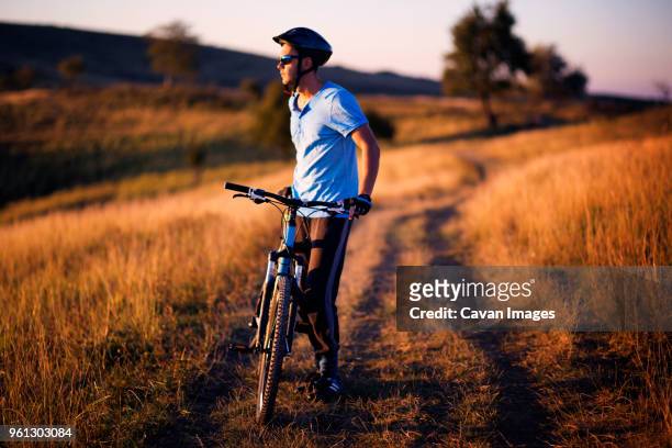 full length of male cyclist standing with bicycle on dirt road field - confidence male landscape stock-fotos und bilder