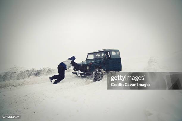 man pushing car on snow field - romanian car stock pictures, royalty-free photos & images