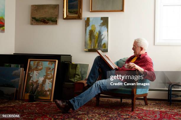 man looking at painting while sitting on armchair - armstoel stockfoto's en -beelden