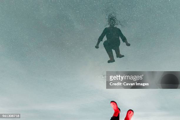 low section of boy reflecting on water while jumping in puddle at street - child and unusual angle stock-fotos und bilder