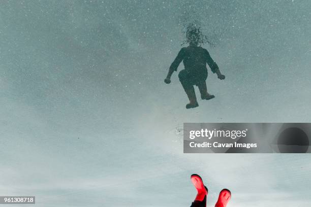 low section of boy reflecting on water while jumping in puddle at street - child and unusual angle stockfoto's en -beelden