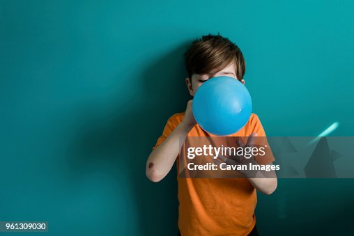 Boy blowing balloon while standing against blue wall at home Boy blowing balloon while standing against blue wall at home