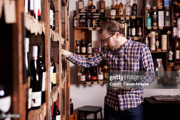 male small business owner examining wine bottle while holding tablet computer in shop - liquor store stock pictures, royalty-free photos & images