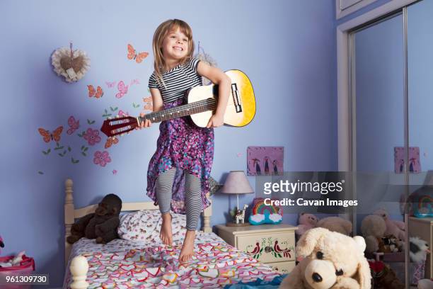 happy girl holding guitar and jumping on bed at home - children holding musical instruments stock pictures, royalty-free photos & images