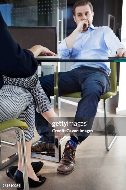 low section of businesswoman playing footsie with male colleague at conference table - playing footsie - fotografias e filmes do acervo