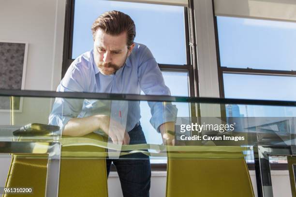 low angle view of businessman analyzing photographs at glass conference table in creative office - redattore iconografico foto e immagini stock