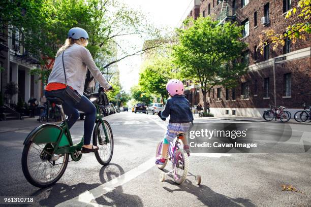 rear view of mother and daughter riding bicycles on street - fietshelm stockfoto's en -beelden