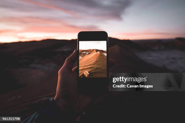 cropped hand photographing sand dunes at beach through smart phone - antofagasta region stock-fotos und bilder