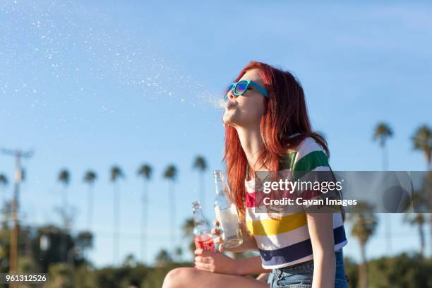 side view of teenage girl spitting drink while sitting against clear sky - spats stock pictures, royalty-free photos & images